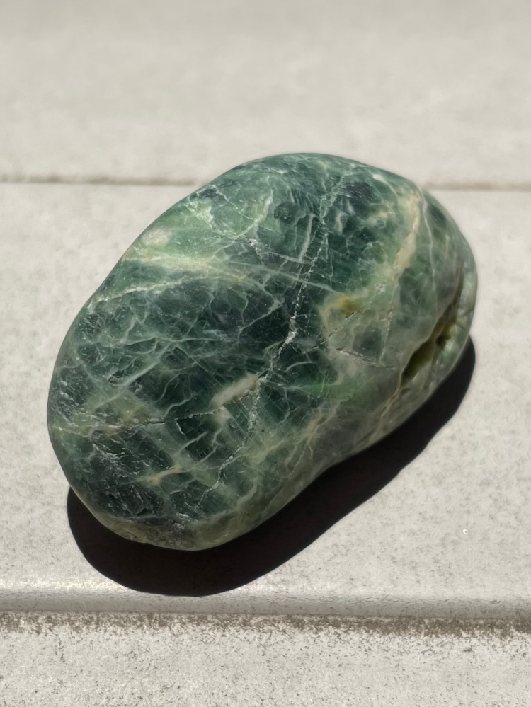 石に詳しい方、教えてください！ この石が何という石なのか気になります。 糸魚川の海岸で拾いました。 特徴としては、 ・全体的に薄緑〜濃緑色。所々白い線が入っている。 ・すべすべしていて、所々石の繊維？スジ？劈開？のようなものが輝いて見える 近くにあったフォッサマグナミュージアムでは鑑定の抽選に外れてしまい、わからないままです…。 よろしくお願いします！