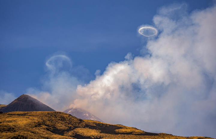 何か珍しいですよね？ イタリア・シチリア島にある活火山としては欧州最高峰のエトナ山から、空に向かって次々とリング状の噴煙が噴き出した。 急激なガスの放出と噴出孔の形状の組み合わせによって発生する現象だとか。
