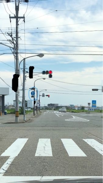 画像の場合どのように動いたら良いか分からないので教えてください。 画像の奥側の信号も赤になっていますが、この信号はどの車向けの信号でしょうか？ 手前の横断歩道奥から左折・右折してきた車は、この場合奥の信号前で停止しなくても良いのでしょうか？ ちなみに奥の信号は奥側の横断歩道の手前にあります。 また手前の信号下の青丸のトラックの標識はどのような意味でしょうか？