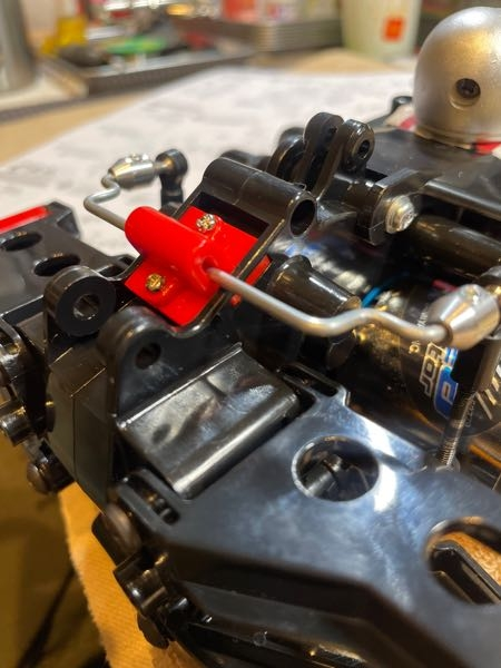 タミヤ スーパーホットショットのスタビライザーについて 写真のようにスタビライザーのバーが下になってしまっています。 指で動かせば簡単に上に行くのですが離すと下に下がってしまいます。 指でバーを上に保持しながらサスを動かすと両方バンザイ状態になるのでスタビライザーの効果が出ていると思うのですが（スタビライザーの効果をあまりよく知らないですが笑）、説明書を見る限り赤いパーツを付けるだけの指示になってます。 このマシンはこれが正常なのでしょうか？ それともバーを固定する何かがあるのでしょうか？ 詳しい方教えてください。